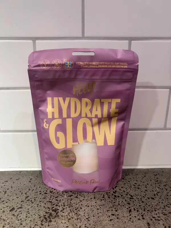 Heey Hydrate & Glow Passion Fruit, lila påse med guldfärgad text